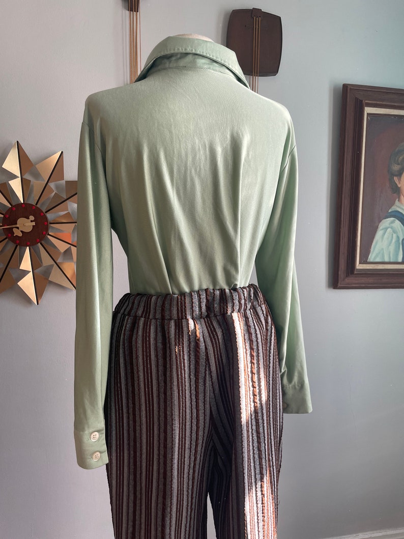 May include: A light green long-sleeved shirt with a collared neckline and brown and white striped trousers.