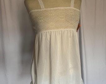 May include: A white slip dress displayed on a mannequin. The bodice has a floral lace design, with delicate straps. The dress is made of a flowing, lightweight fabric and has a ruffled hemline, creating a vintage aesthetic.