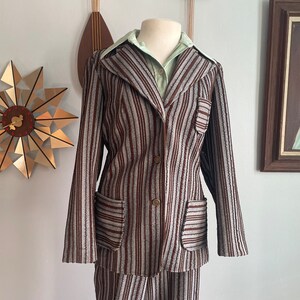 May include: A striped brown and grey trouser suit with a collared jacket and long sleeves. The jacket has two pockets and a button fastening.