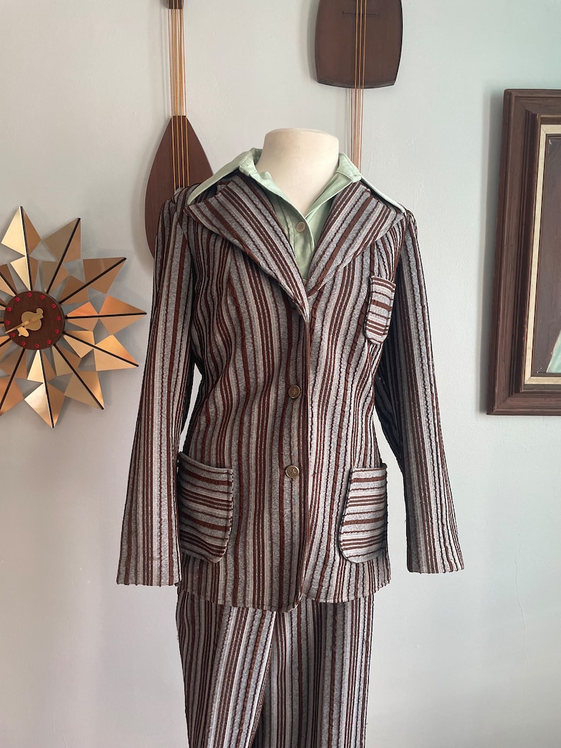 May include: A striped brown and grey trouser suit with a collared jacket and long sleeves. The jacket has two pockets and a button fastening.