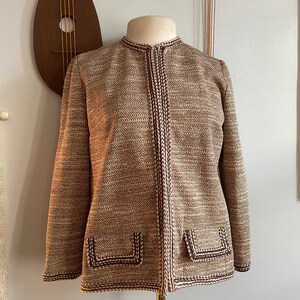 May include: A brown and white tweed jacket with brown trim and pockets. The jacket has a mandarin collar and a front zipper closure.