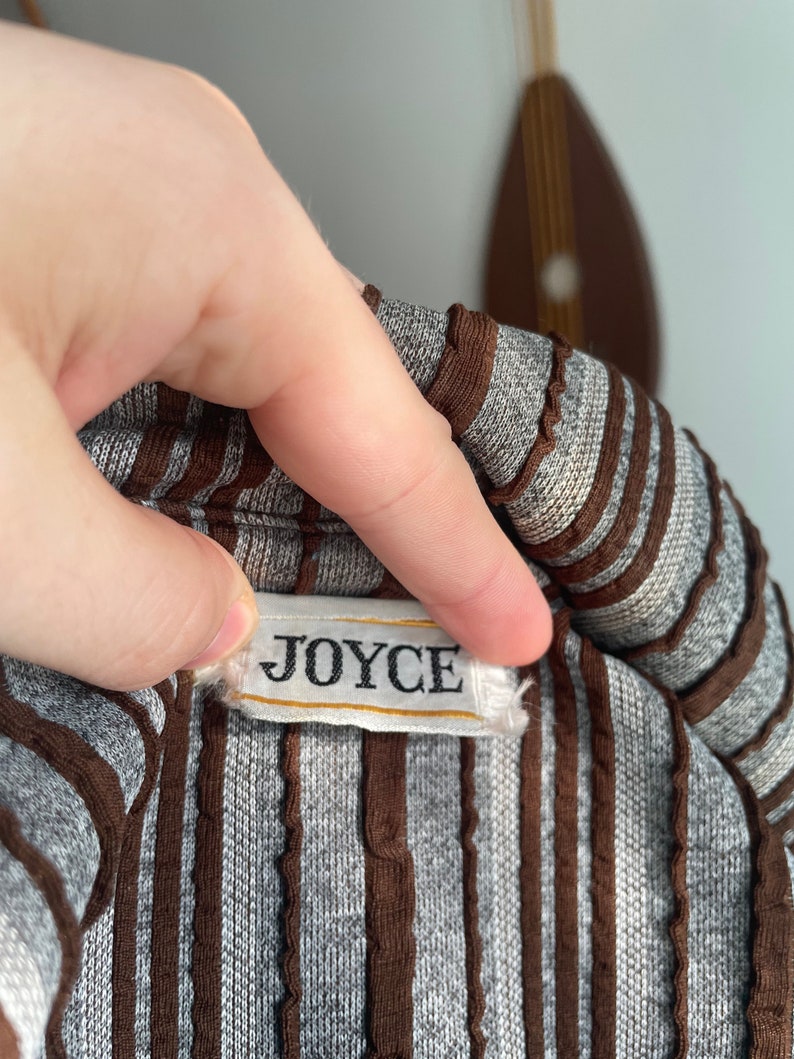 May include: A close-up of a brown and grey striped shirt with a white label that reads "JOYCE".