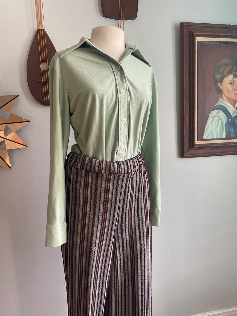 May include: A light green long-sleeved button-down shirt with a collared neckline and brown and grey striped trousers.