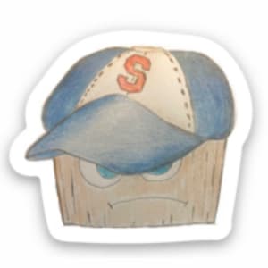 May include: A cartoon illustration of a wooden cupcake wearing a blue baseball cap with a red "S" on the front. The cupcake has a grumpy expression with furrowed brows and a frown.