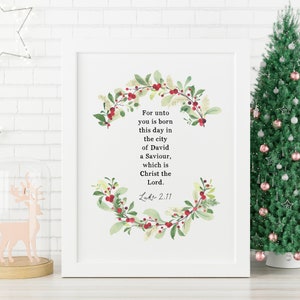 May include: A white framed print with a watercolor wreath of green leaves and red berries. The print features a Christmas-themed quote from the Bible: "For unto you is born this day in the city of David a Saviour, which is Christ the Lord. Luke 2:11"