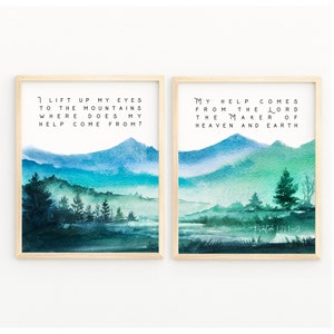 Könnte beinhalten: Zwei gerahmte Aquarelldrucke mit Berglandschaften in Blau- und Grüntönen. Der linke Druck zeigt den Text "I lift up my eyes to the mountains where does my help come from?". Der rechte Druck hat den Text "My help comes from the Lord the maker of heaven and earth."