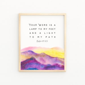 May include: A framed print with the text "Your Word is a lamp to my feet and a light to my path Psalm 119:105." The artwork features a watercolour landscape in shades of purple, pink, and yellow, with a light wooden frame.