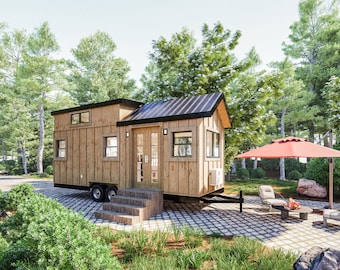 May include: A small, wooden, single-story house on wheels with a black metal roof. The house has a large front door with glass panels and a small porch with steps. The house is parked on a gravel driveway in a wooded area. There is a red umbrella and patio furniture in front of the house.
