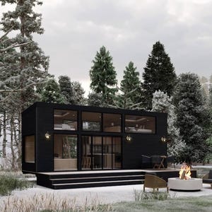 May include: A modern black cabin with large windows, nestled in a snowy forest. The cabin features a deck, outdoor seating, and a fire pit. The scene is set against a backdrop of snow-covered trees and a cloudy sky.