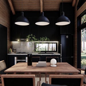May include: Interior shot of a modern kitchen and dining area. The space features a wooden table and chairs, black pendant lights, and a black kitchen with a refrigerator. Large windows offer a view of trees and natural light.