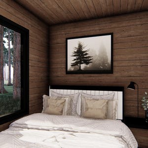 May include: A cozy bedroom with wood-paneled walls and ceiling. A large window offers a view of a forest. The bed has a white comforter and pillows. A framed picture of a tree hangs above the bed. A black nightstand and lamp are visible.