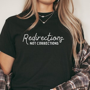May include: A black t-shirt with the text "Redirections not corrections" in white lettering. The shirt is being worn by a person with long blonde hair.