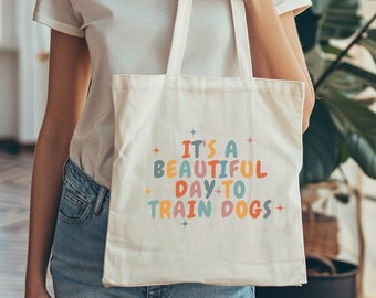 May include: A white canvas tote bag with the text "It's a beautiful day to train dogs" in colorful letters. The text is surrounded by small stars.