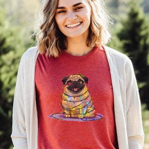 May include: A red t-shirt with a cartoon pug wearing Christmas lights. The pug is brown and white with a black nose and tongue. The lights are multi-colored and wrapped around the pug's body.