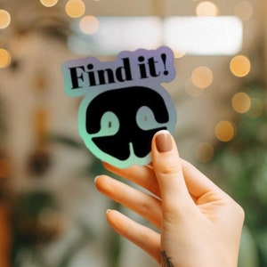 以下が含まれることがあります： 黒い生き物のシルエットと「Find it!」という黒い文字が書かれたホログラフィックステッカーです。