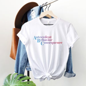 Könnte beinhalten: Weißes T-Shirt mit dem Text "Antezedenz Verhalten Konsequenz" in einem Blau- und Rosaton-Verlauf.