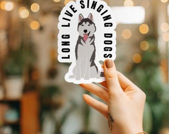 May include: White sticker with a black and white illustration of a husky dog sitting with its tongue out. The text "Long Live Singing Dogs" is written in a semi-circle around the dog.