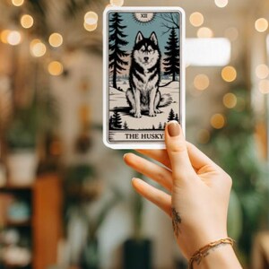May include: A tarot card with a black and white illustration of a husky dog sitting on a snowy background. The card is labeled "The Husky" and has the Roman numeral XII in the top right corner.