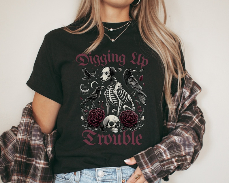 May include: Black t-shirt with a graphic design of a skeleton dog with crows and flowers. The text "Digging Up Trouble" is printed in a gothic font.
