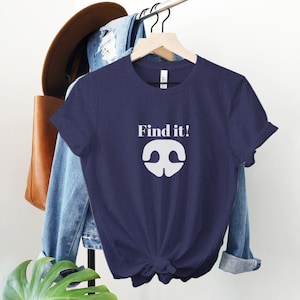 May include: A navy blue t-shirt with a white graphic of a nose and the text "Find it!" printed on the front.