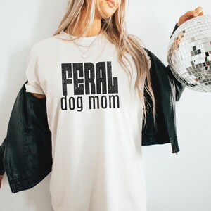 May include: White t-shirt with black text that reads "FERAL dog mom".