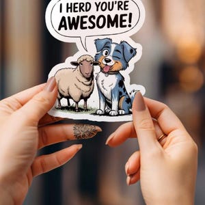 Peut inclure: Un autocollant avec un chien et un mouton de dessin animé. Le chien est bleu et blanc avec un nez noir et la langue qui sort. Le mouton est blanc avec un nez noir. L'autocollant a une bulle de dialogue qui dit "I herd you're awesome!"