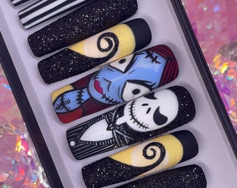 Puede incluir: Un conjunto de uñas postizas en forma de ataúd con una variedad de diseños. Algunas uñas presentan rayas blancas y negras, mientras que otras muestran personajes de The Nightmare Before Christmas, incluyendo a Jack Skellington y Sally.