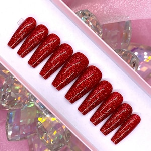 Pode incluir: Conjunto de dez unhas postiças longas de caixão vermelhas com glitter em uma caixa branca.