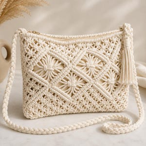 May include: An off-white macrame crossbody bag featuring a complex diamond knot pattern, a solid inner lining, a top zipper closure, a braided shoulder strap, and a decorative tassel attached to the side of the bag's upper corner.
