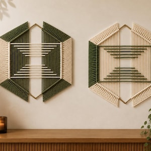 Peut inclure: Deux décorations murales hexagonales composées de cordes en macramé aux tons vert olive et crème. Chaque pièce est structurée autour d'un cadre en métal doré, présentant un motif symétrique avec des cordes horizontales au centre.