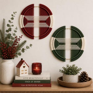 May include: Two circular wall hangings featuring dark red and dark green cord wrapped around gold metal frames with cream-colored horizontal thread patterns. The designs are symmetrical, split into two halves with a central open space between them.