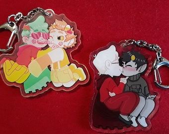 May include: Two acrylic keychains featuring cartoon characters in affectionate poses. One keychain shows two figures embracing, while the other depicts two figures kissing. Each keychain has a silver-colored clasp.