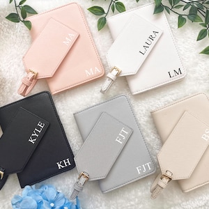 May include: Five passport holders with matching luggage tags. Each passport holder is a different color: pink, white, black, gray, and beige. The luggage tags have the initials of each holder's name: MA, LM, KH, FJT, and BS.
