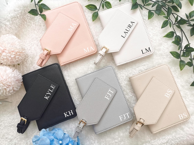 May include: Five passport holders with matching luggage tags. Each passport holder is a different color: pink, white, black, gray, and beige. The luggage tags have the initials of each holder's name: MA, LM, KH, FJT, and BS.