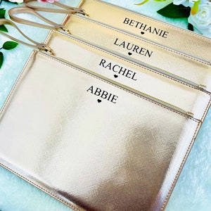 May include: Four gold-colored zippered pouches with black handles and black text. The pouches are stacked on top of each other. The text on the pouches reads "Bethanie", "Lauren", "Rachel", and "Abbie".