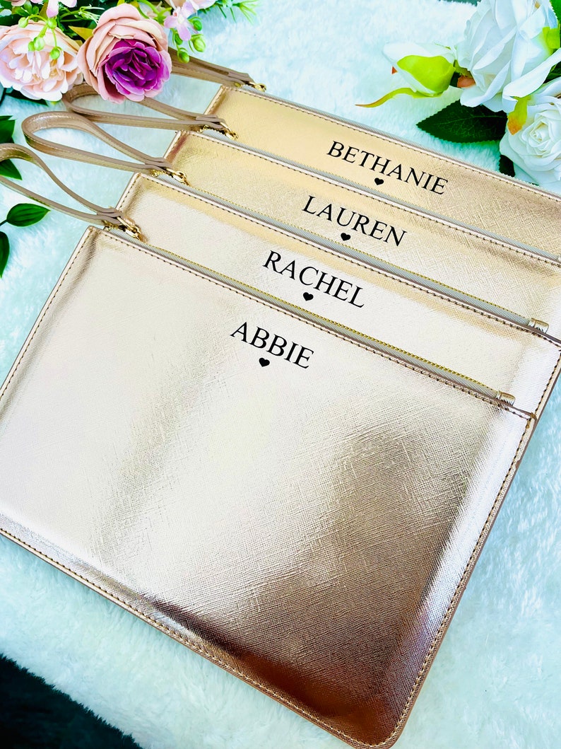 May include: Four gold-colored zippered pouches with black handles and black text. The pouches are stacked on top of each other. The text on the pouches reads "Bethanie", "Lauren", "Rachel", and "Abbie".