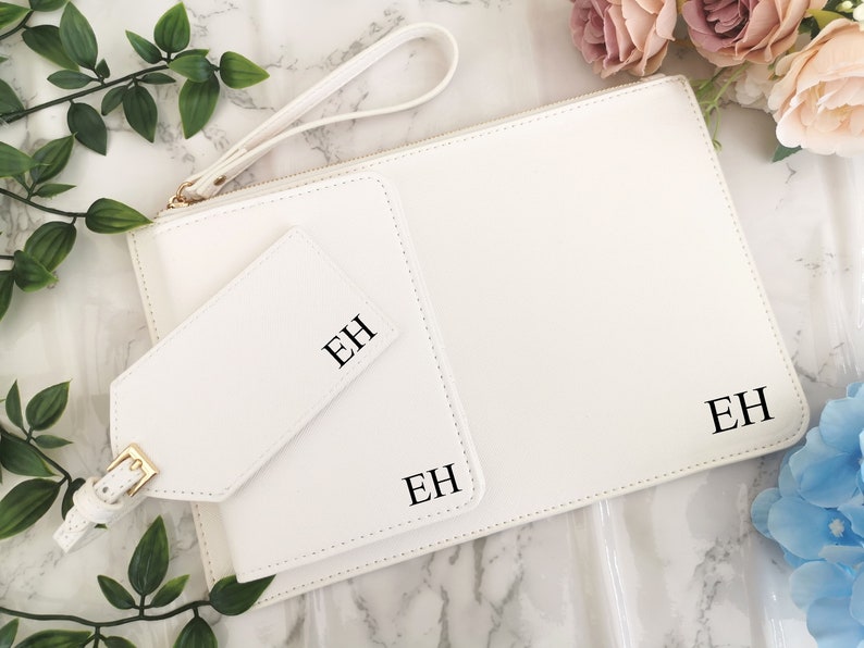 May include: White leather clutch with a matching luggage tag. Both items have the initials "EH" embossed in black.