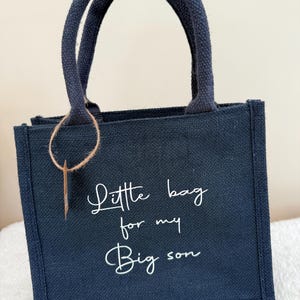 May include: A navy blue tote bag with matching handles and the text "Little bag for my Big son" in white script. The bag has a rectangular shape and a small, rectangular tag attached to the handle.