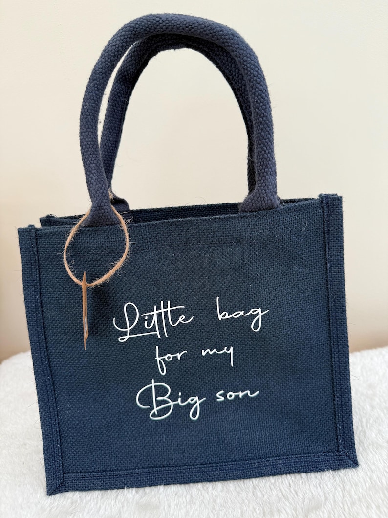 May include: A navy blue tote bag with matching handles and the text "Little bag for my Big son" in white script. The bag has a rectangular shape and a small, rectangular tag attached to the handle.