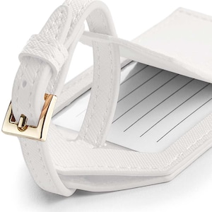 May include: White leather luggage tag with a gold buckle and a flap that opens to reveal a writing area.