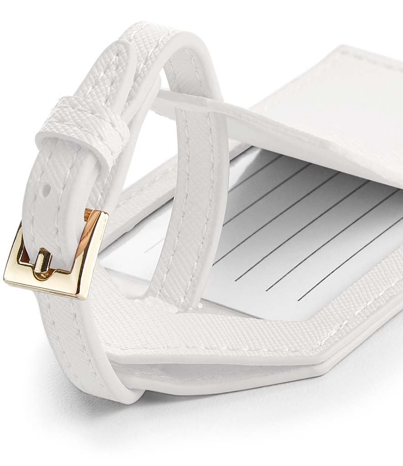 May include: White leather luggage tag with a gold buckle and a flap that opens to reveal a writing area.