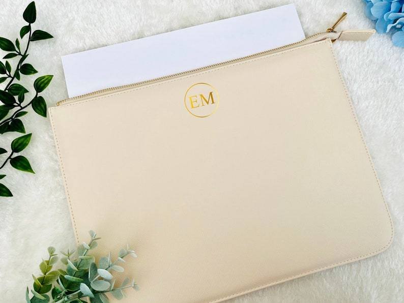 May include: A cream-colored zippered pouch with a gold circle and the initials "EM" in gold lettering.