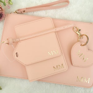 May include: A pink leather clutch with a matching pink leather luggage tag and key chain. The clutch has a gold zipper and the luggage tag and key chain have gold hardware. The luggage tag and key chain are personalized with the initials "MM".