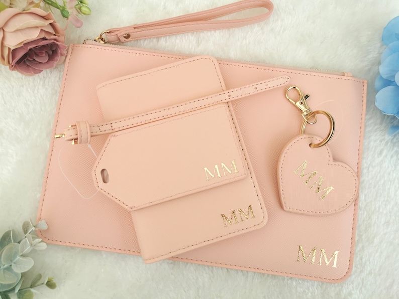 May include: A pink leather clutch with a matching pink leather luggage tag and key chain. The clutch has a gold zipper and the luggage tag and key chain have gold hardware. The luggage tag and key chain are personalized with the initials "MM".