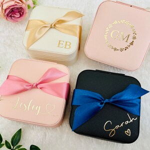 K&ouml;nnte beinhalten: Vier quadratische Schmuckk&auml;stchen in verschiedenen Farben mit personalisierten Namen. Die K&auml;stchen sind rosa, wei&szlig;, schwarz und hellrosa. Die Namen auf den K&auml;stchen sind "EB", "GM", "Lesley" und "Sarah".