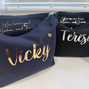 May include: A navy blue pouch with the name Vicky in gold foil and a small gold heart, and a black pouch with the name Teresa in silver foil and a small silver heart. Both feature interior text reading We love you! Elisha and Josiah.