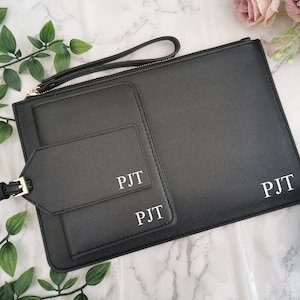 May include: Black leather travel pouch with two zippered pockets and a luggage tag. The pouch and tag are personalized with the initials "PJT".