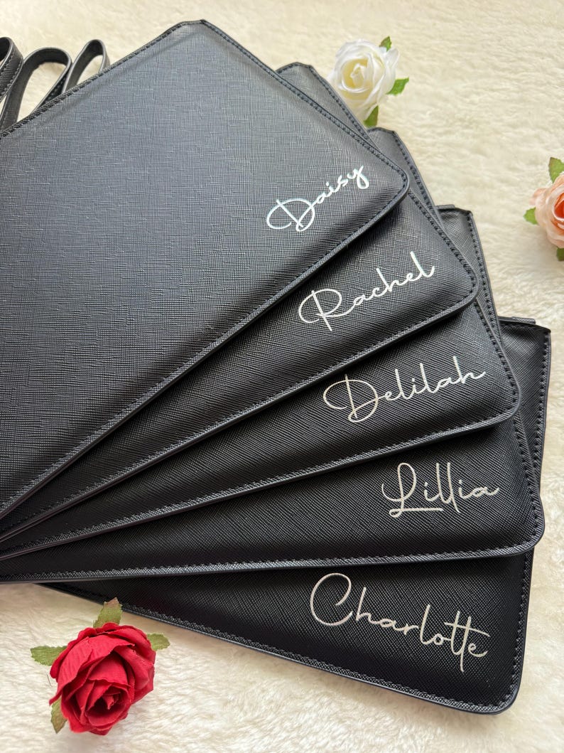 May include: A stack of five black rectangular pouches with a textured finish. Each pouch features a white script name printed on the front: Daisy, Rachel, Delilah, Lillia, and Charlotte. The pouches are arranged in a fan shape.