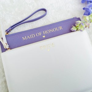 May include: Two purple and white zippered pouches with gold lettering. The top pouch says "Maid of Honour" and the bottom pouch says "Bride".
