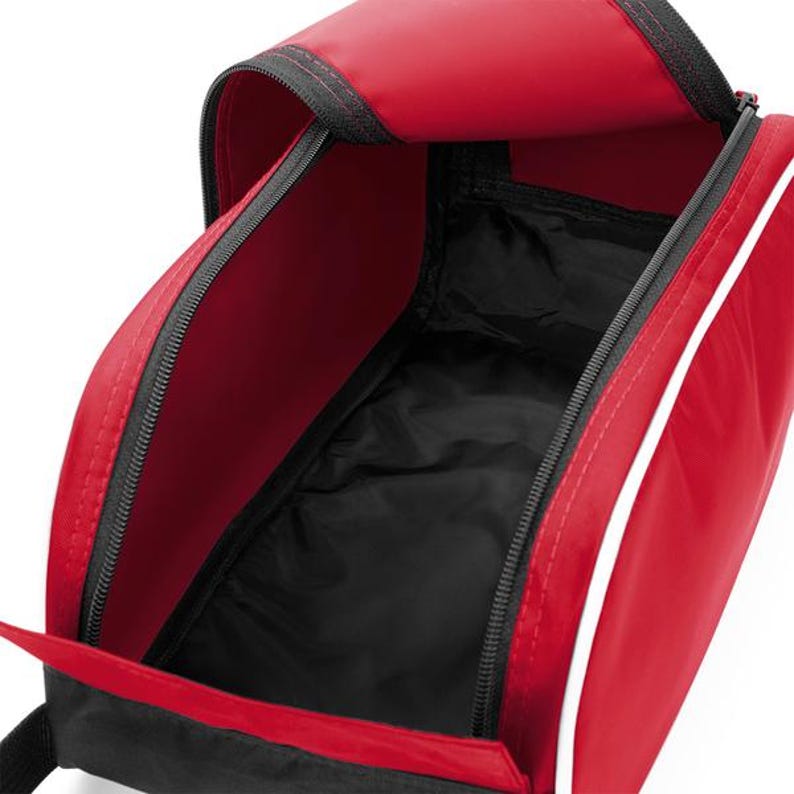 May include: A red and black zipped shoe bag with a wide opening. The exterior is primarily red with a thin white piping detail along the side. The interior is lined with black fabric, and the bag features a black base and black zip tracks.